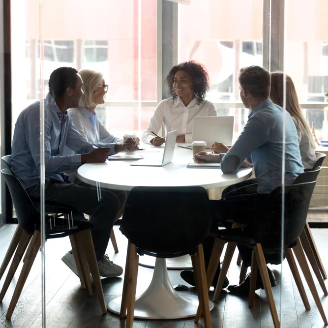 African American boss with employees sitting at desk in boardroom, businesswoman with colleagues discussing business strategy or project together, using laptops, brainstorm or company meeting