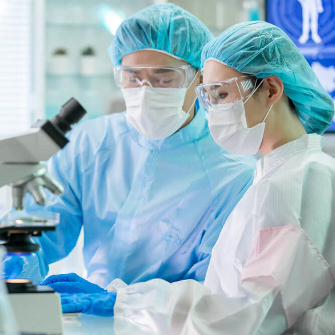 Biotech lab technicians looking into microscope wearing scrubs