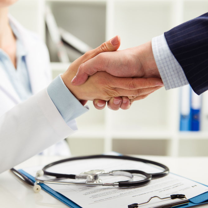 Woman doctor shaking hand with businessman in office