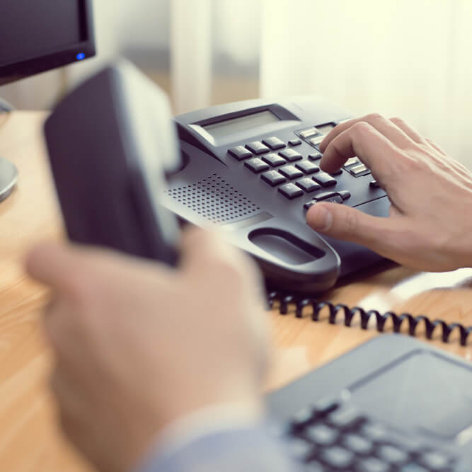 Businessman dialing phone number on corporate desk phone close up on hand